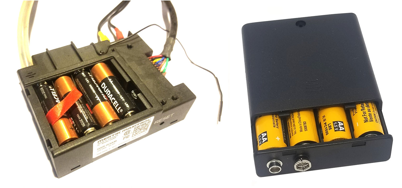 Two separate components related to a fireplace control system. On the left is a black fireplace control module with multiple wires of different colors protruding from one side. It houses four AA batteries arranged in a 2x2 configuration. On the right is a separate black battery holder designed for four AA batteries, arranged in a single row. The battery holder has a positive and negative terminal next to each other at one end.