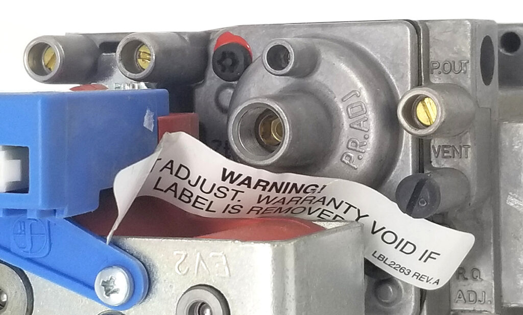 Close-up image of a gas valve assembly, highlighting various ports labeled P.OUT, VENT, and P.R.ADJ. A warning label is partially peeled off, indicating that the warranty is void if the label is removed. The blue component on the left side is part of the assembly.
